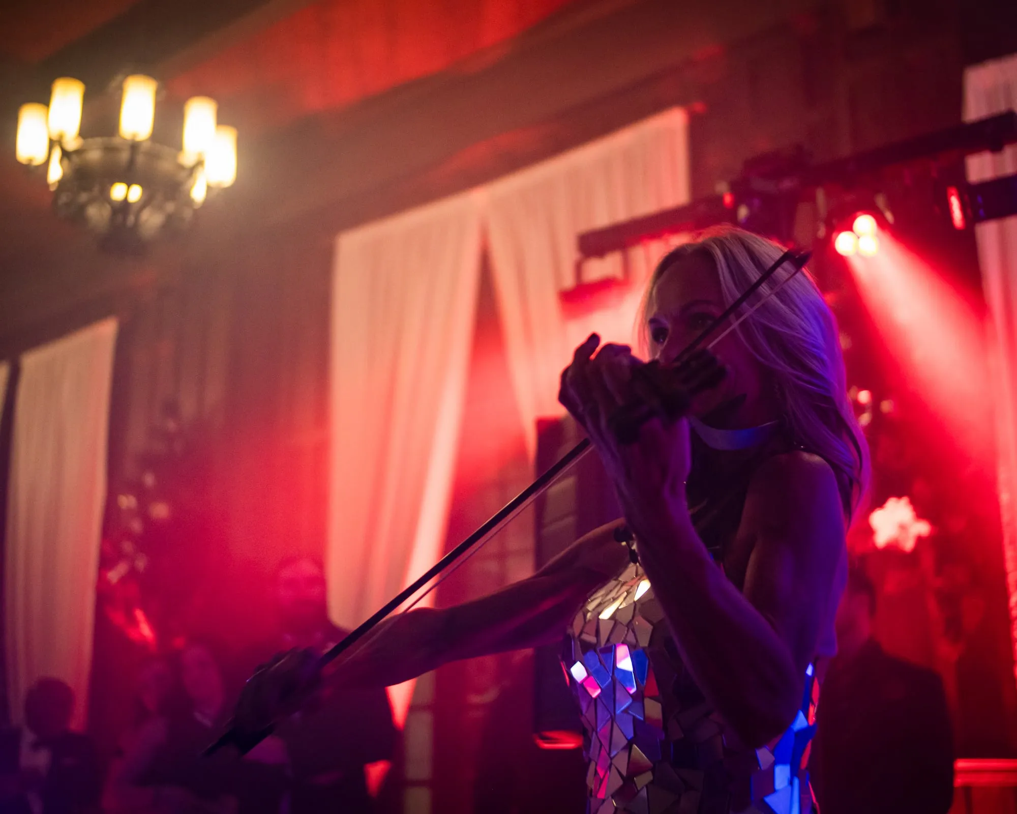 A violinist performs under dramatic stage lighting at the Denver Winter Ball