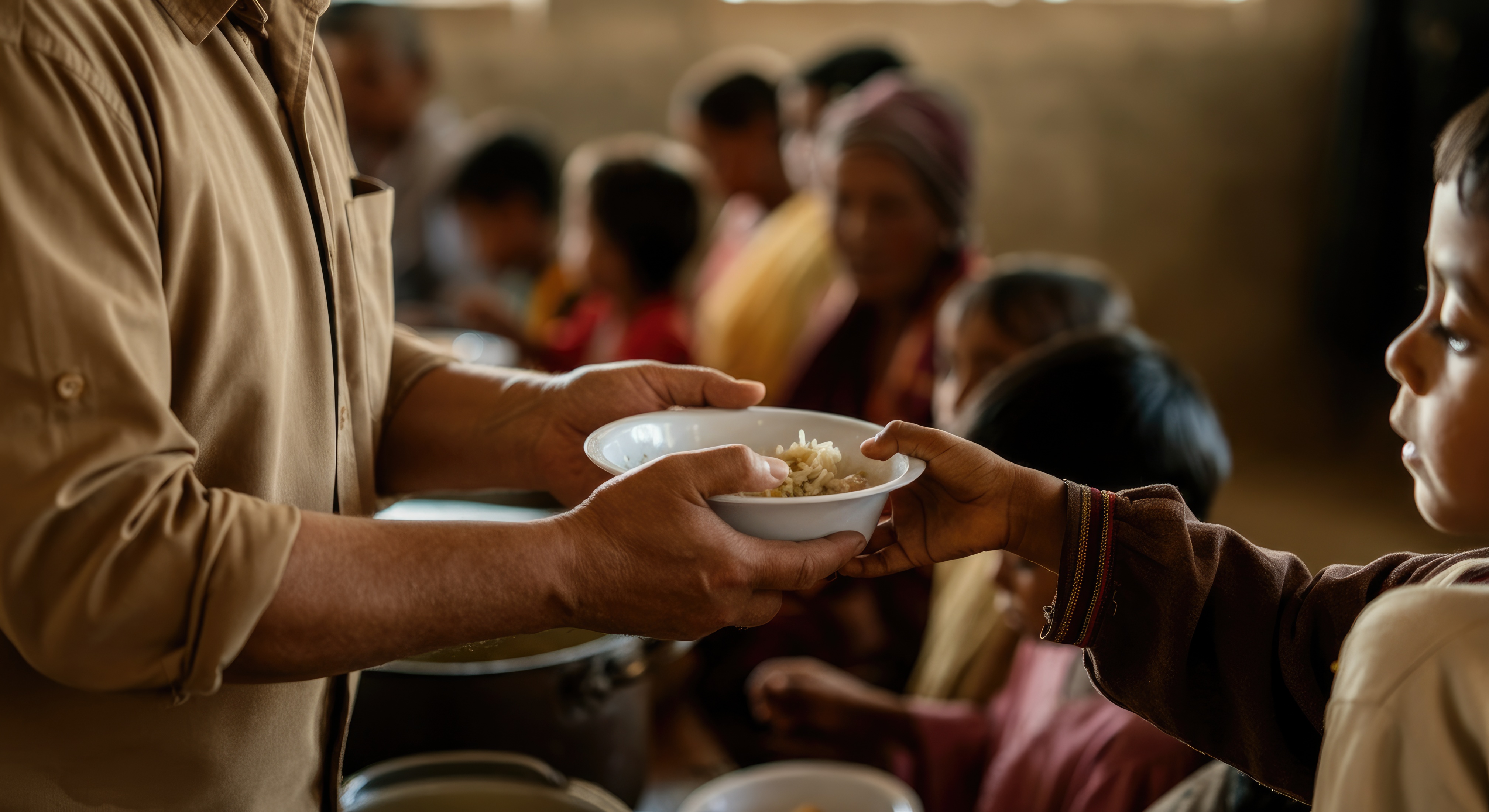 A volunteer hands a bowl of food to a child waiting in line at a community meal